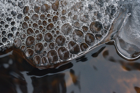 The accumulation of air bubbles under the thin crust of ice against the background of a turbulent flow of water.の写真素材