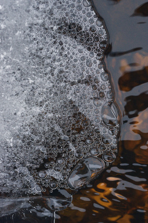 The accumulation of air bubbles under the thin crust of ice against the background of a turbulent flow of water.の写真素材