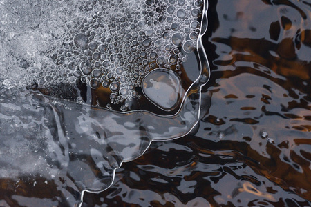 The accumulation of air bubbles under the thin crust of ice against the background of a turbulent flow of water.の写真素材