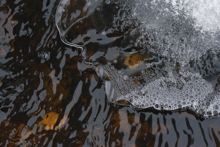 The accumulation of air bubbles under the thin crust of ice against the background of a turbulent flow of water.の写真素材