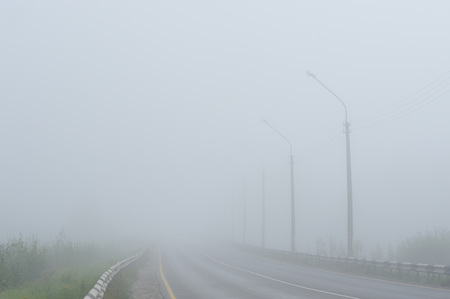 An empty road disappearing into the dense morning fog.の写真素材