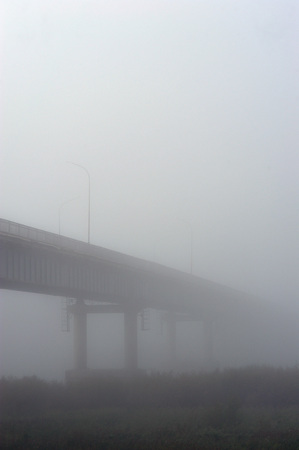 Bridge over the river during a dense morning fog disappearing in it.の写真素材