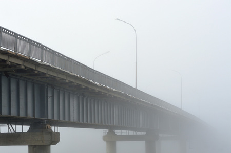 Bridge over the river during a dense morning fog disappearing in it.の写真素材