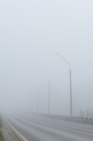 An empty road disappearing into the dense morning fog.の写真素材