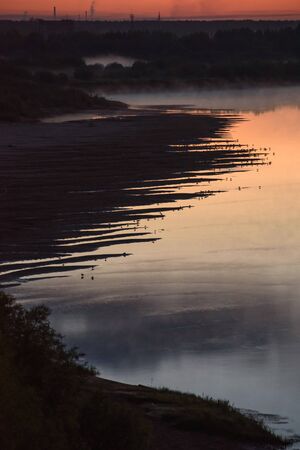 Night on the banks of the river with rising fog and a lot of birds sitting at the edge of the water on the shore.の写真素材