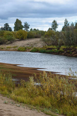 A picturesque river bank in early autumn with grass on the bank changing its color from green to yellow.の写真素材