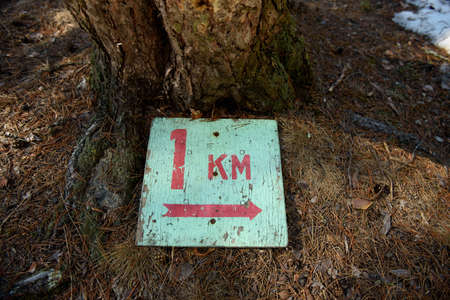 A sign indicating the length of the tourist route 1 kilometer lying on the ground thawed from snow...