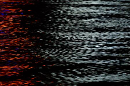 Blurred colorful light on river surface with water waves in the dark night for background backdropの写真素材