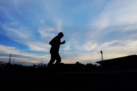 Silhouette scene of a male walking on the road lane at the stadium against blue sky white clouds at...