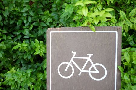 A woonden bicycle signboard with green leaves background in outdoor spaceの写真素材
