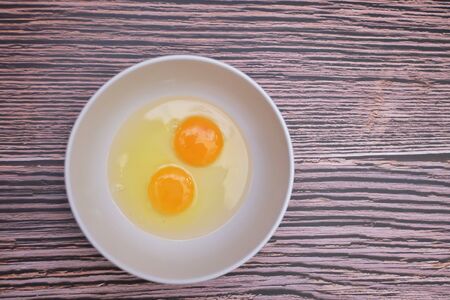 In selective focus top view of a fresh egg in a white bowlon old wooden table background with copy spaceの写真素材