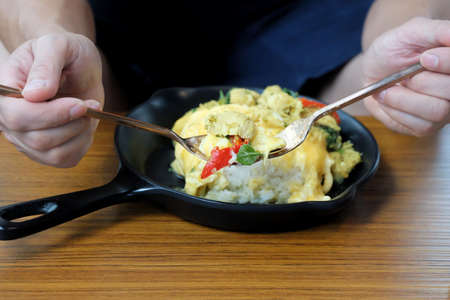A male hand holding a spoon of green curry chicken with cooked rice and blurred a black plate on...
