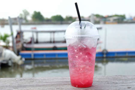 A bottle of sweet iced red cocktail on old wooden balconyin outdoor space,blurred a boat in a river and water viewの写真素材