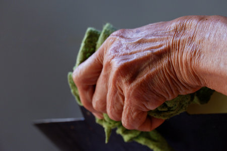 In selective focus a wrinkle hand of old woman holding a blurred black pan in a kitchen areaの写真素材