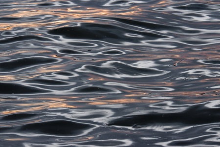 Blurred colorful light reflection on river surface with water waves in the dark night backgroundの写真素材