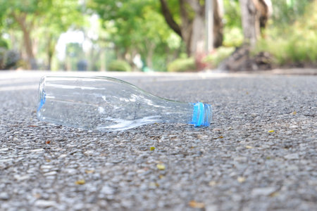 An empty of drinking plastic bottle littering on the ground floor in plubic park road with blurred...