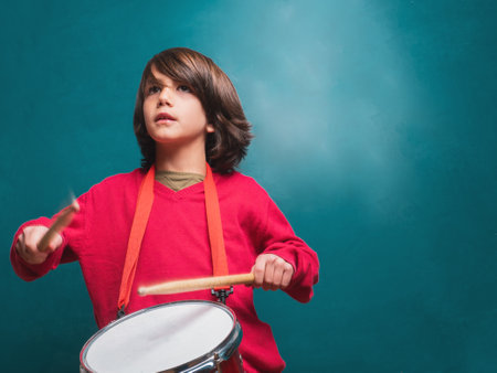 Boy with red sweater playing drum in front of a school blackboardの写真素材