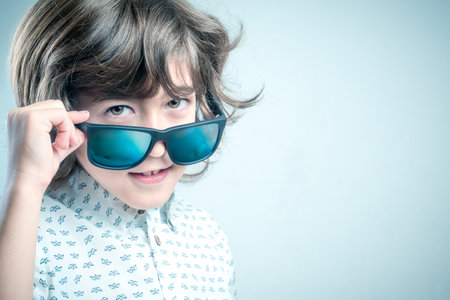 Boy in white shirt with blue details posing in a photo shoot with sunglasses.の写真素材