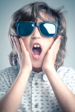 Boy in white shirt with blue details posing in a photo shoot with sunglasses.の写真素材