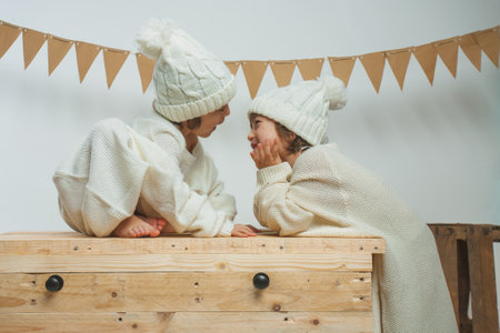 Photo session with twins dressed in white sweaters and wool caps posing and playing with confetti.の写真素材