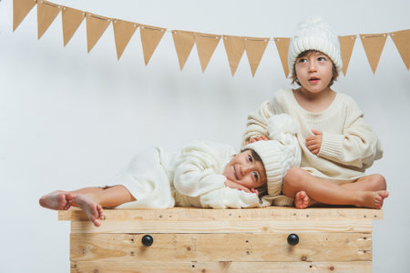 Photo session with twins dressed in white sweaters and wool caps posing and playing with confetti.の写真素材