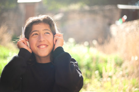 Boy listening to music with white headphones outside next to a green meadow.の写真素材