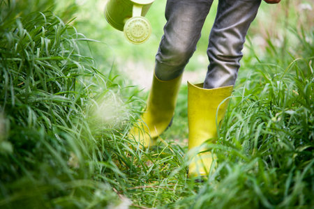 Boy walking with his wellies and a watering can in a grassy meadow. Conceptual image that can represent Earth Day and Environment Day.の写真素材