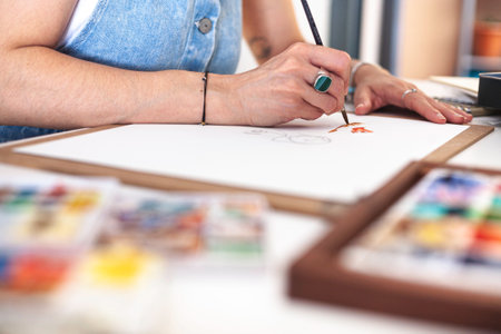 Selective focus on the hands of an illustrator painting her work among the different watercolor...