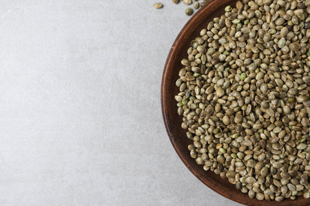 There is a clay bowl with hemp seeds on the concrete surface. Horizontal orientation.