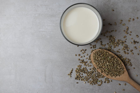 A wooden spoon with hemp seeds and a glass of hemp milk stand on a concrete surface. Food background.の写真素材