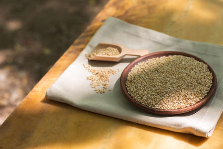 Brown sesame seeds in a clay bowl on a wooden table.の写真素材
