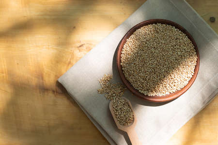 Brown sesame seeds in a clay bowl on a wooden table.の写真素材