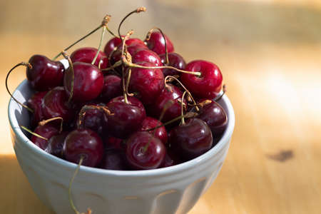 A bowl of ripe cherries is on a wooden table.の写真素材
