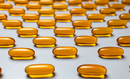 Yellow capsules omega-3 on a gray background. Pattern. Pantone colors of 2021.の写真素材
