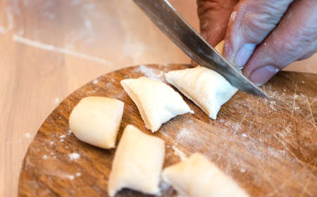 Female hands cut pieces of dough for dumplings with a knife on a wooden board.の写真素材