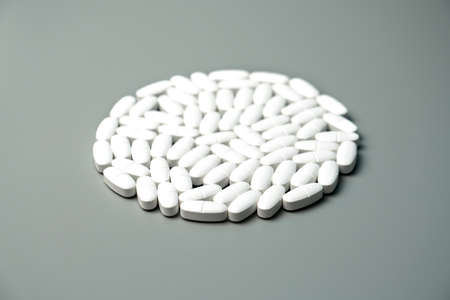 Calcium capsules with vitamin D on a gray background in the shape of a circle. Medical background.の写真素材