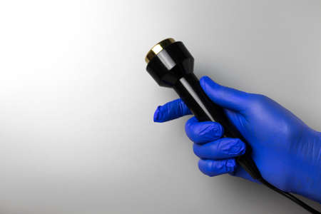 A hand in a blue glove holds a handpiece for ultrasonic massage. Gray background with place for text.の写真素材