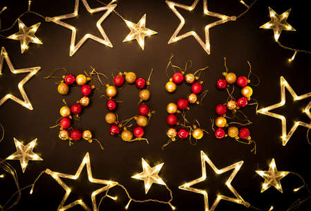 Christmas balls of red and gold on a black background are laid out in the form of the number 2022. Around the number 2022 there is a Christmas tree gardend in the form of stars.の写真素材