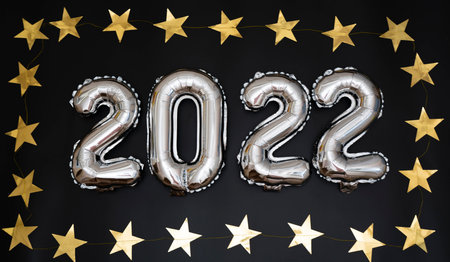 Silver balloons on a black background are laid out in the form of the number 2022. Around the number...