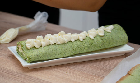 A woman decorates a pistachio roll with cream. Master class on cooking desserts. high quality photoの写真素材