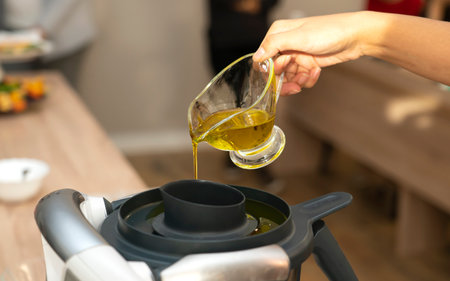 Master class in cooking. A cook pours oil into a food processor (blender) to make a salad dressing. high quality photoの写真素材