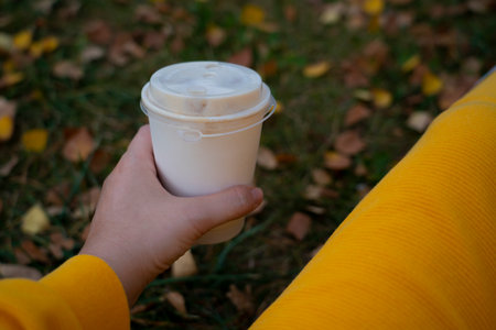 A paper cup with coffee in the hands of a woman against the backdrop of an autumn landscape. high quality photoの写真素材