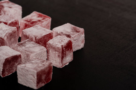 Turkish traditional dessert - lokum with rose flavor. Red cubes of Turkish delight in powder on a black background. high quality photoの写真素材