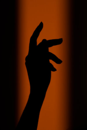 Silhouette, shadow of a woman's hand on the wall in the orange rays of the setting sun. Abstract background in blur, out of focus. high quality photoの写真素材