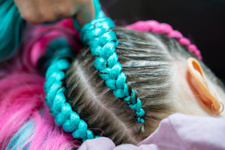 Fashionable hairstyle for a girl from pink and blue kanekalon braids. The hairdresser weaves braids...