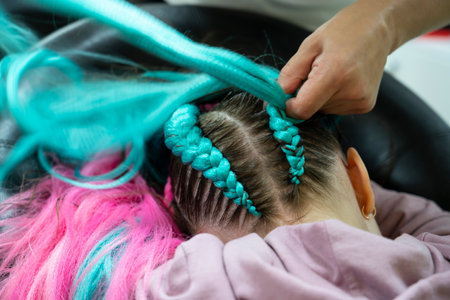 Fashionable hairstyle for a girl from pink and blue kanekalon braids. The hairdresser weaves braids...