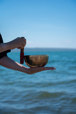 A singing (Tibetan) bowl in the hands of a girl against the background of the blue water of the...