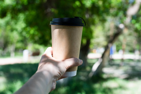 A brown glass with a takeaway cappuccino in the hands of a woman against the backdrop of nature. high quality photoの写真素材