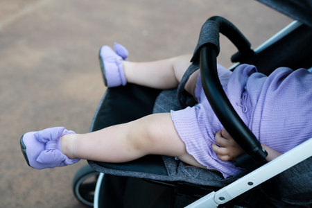The legs of a girl lying in a stroller close-up. The color of the child's clothes and shoes is...