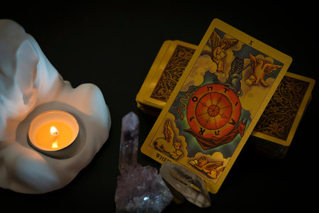 Gold embossed tarot cards, candle in a plaster candlestick and natural crystals on the table. The Major Arcana card The Wheel of fortune lies facing the viewer. high quality photoの写真素材